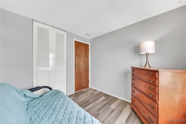 bedroom featuring light wood-type flooring, baseboards, and a closet