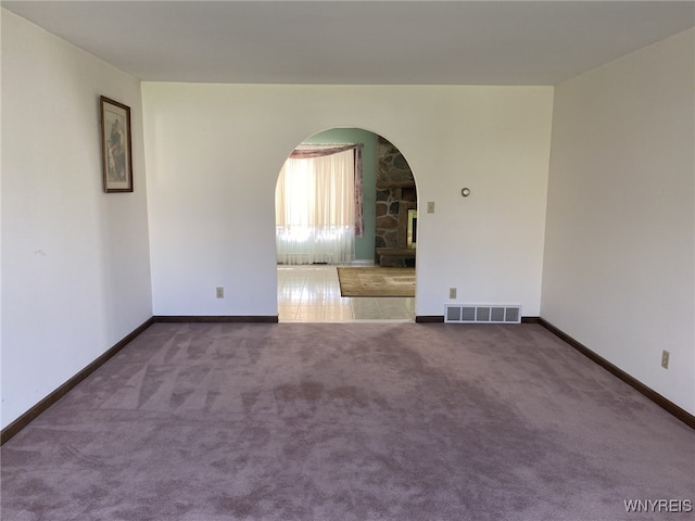 carpeted empty room featuring visible vents, arched walkways, and baseboards