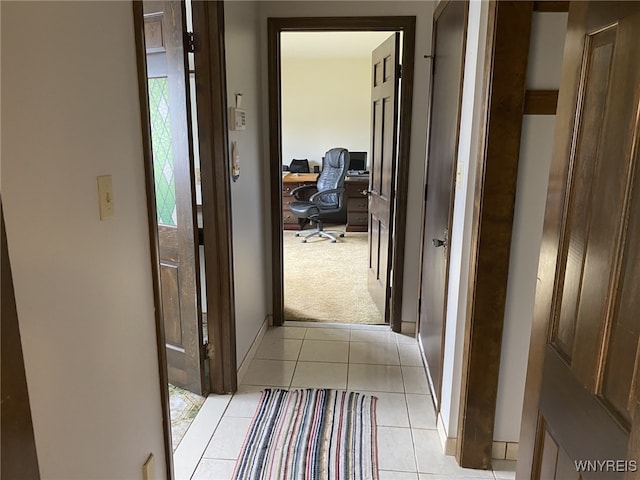 hall with baseboards, light tile patterned floors, and light carpet