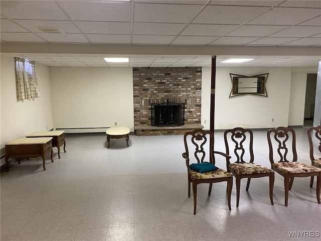finished below grade area featuring a fireplace, tile patterned floors, baseboard heating, and a drop ceiling
