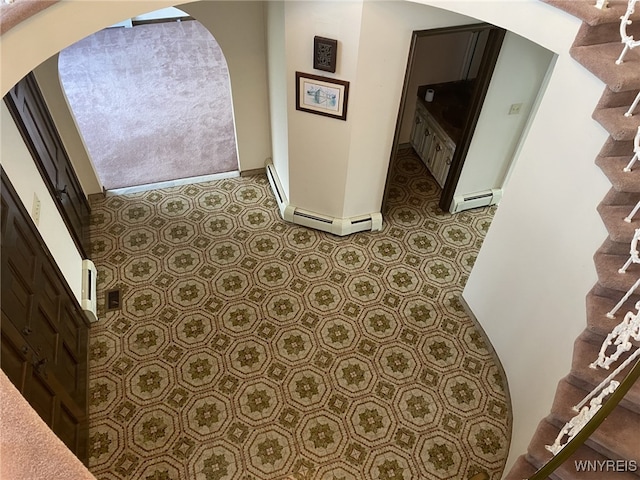 hallway with arched walkways, tile patterned floors, stairs, baseboards, and a baseboard heating unit