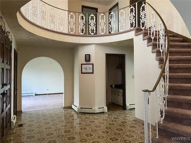 carpeted foyer entrance featuring arched walkways, baseboards, baseboard heating, and a towering ceiling