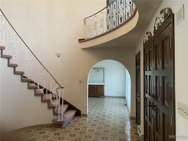 entrance foyer featuring arched walkways, tile patterned floors, a baseboard radiator, visible vents, and stairway