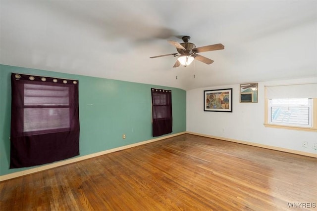 empty room with baseboards, ceiling fan, vaulted ceiling, and wood finished floors