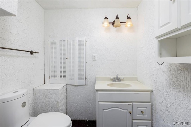 bathroom with vanity, a textured wall, and toilet