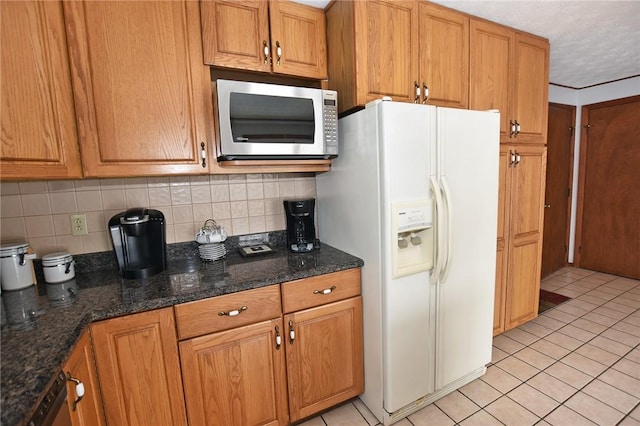 kitchen featuring stainless steel microwave, light tile patterned floors, white refrigerator with ice dispenser, and tasteful backsplash