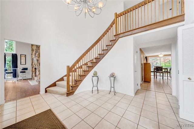 staircase featuring tile patterned flooring, a towering ceiling, a notable chandelier, and a wealth of natural light