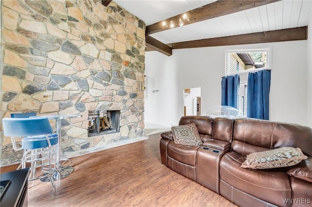 living room featuring beamed ceiling, a stone fireplace, and wood finished floors