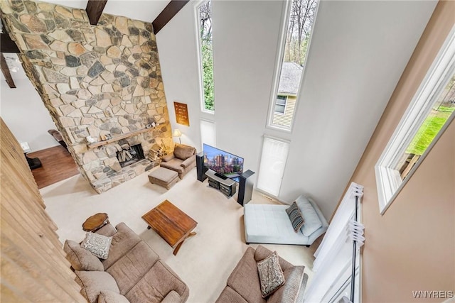 living room featuring a healthy amount of sunlight, a fireplace, beam ceiling, and a towering ceiling