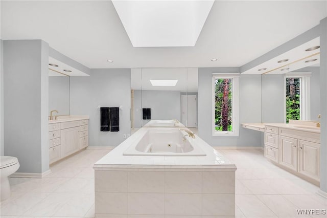 full bath featuring a jetted tub, two vanities, a sink, baseboards, and tile patterned floors