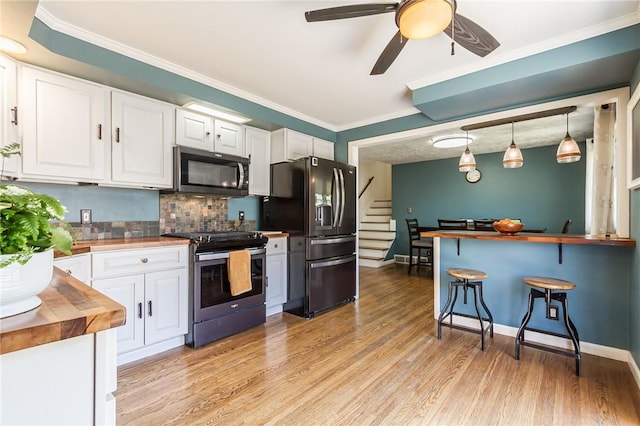 kitchen featuring appliances with stainless steel finishes, a breakfast bar area, white cabinetry, backsplash, and butcher block counters
