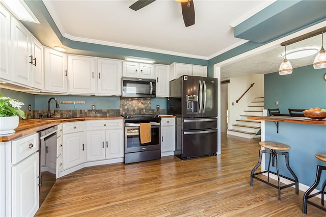 kitchen featuring light wood-type flooring, a sink, wood counters, stainless steel appliances, and white cabinetry