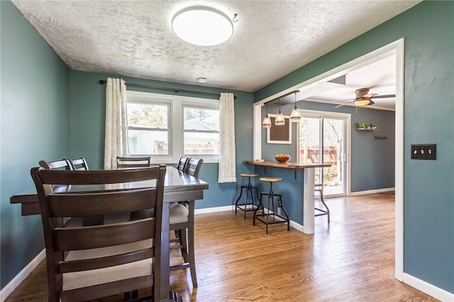 dining space with a textured ceiling, a healthy amount of sunlight, baseboards, and wood finished floors