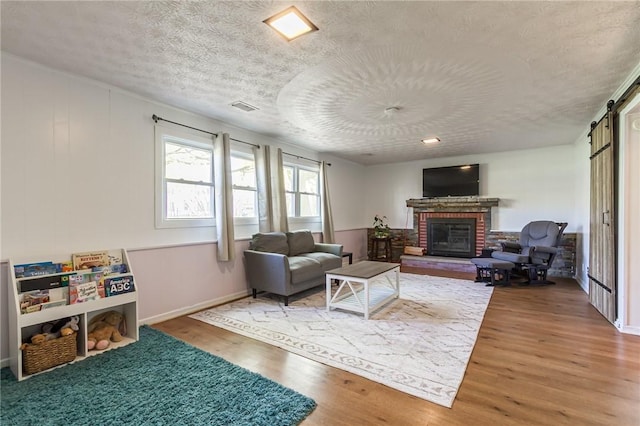 living room with a barn door, a fireplace, a textured ceiling, wood finished floors, and visible vents