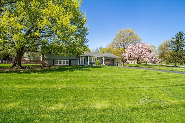 view of front of house featuring an attached garage, a front lawn, fence, and driveway