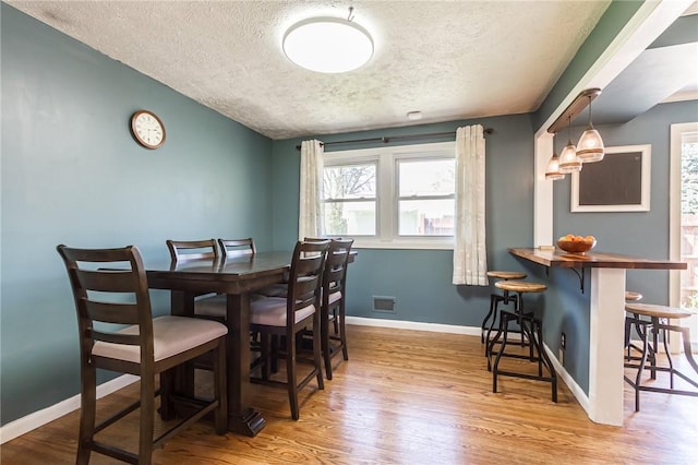 dining area with baseboards, visible vents, a textured ceiling, and wood finished floors