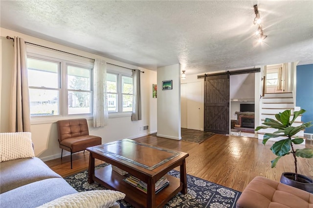 living area featuring baseboards, a barn door, a textured ceiling, and wood finished floors