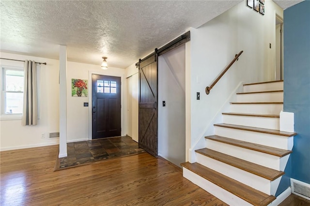 foyer with a textured ceiling, visible vents, wood finished floors, a barn door, and stairway