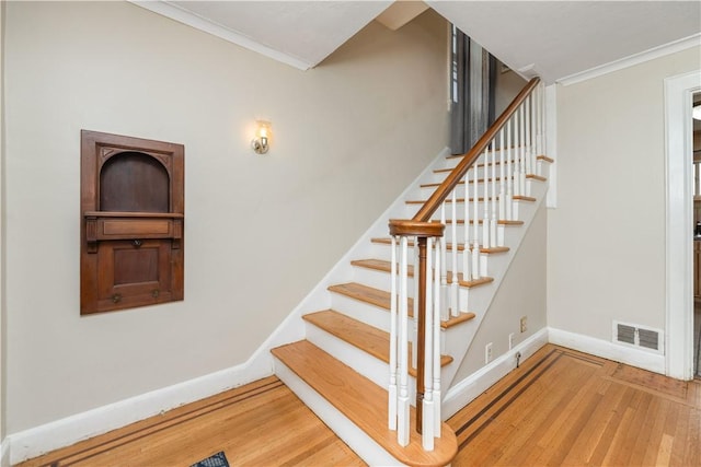 stairway with visible vents, baseboards, crown molding, and wood finished floors