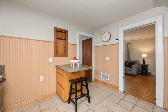 kitchen featuring dark countertops, a wainscoted wall, light tile patterned floors, and visible vents