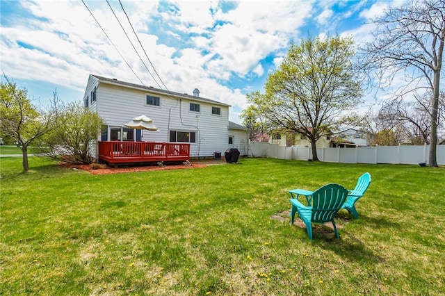 rear view of house featuring a wooden deck, a yard, and fence