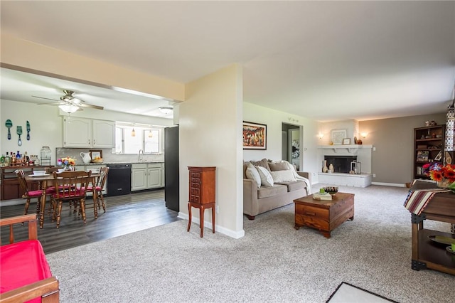 carpeted living area with baseboards, a sink, and a ceiling fan