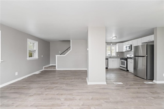 unfurnished living room with stairs, baseboards, a sink, and light wood-style flooring