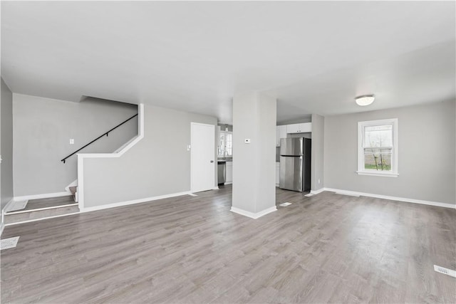unfurnished living room with baseboards, wood finished floors, and stairway