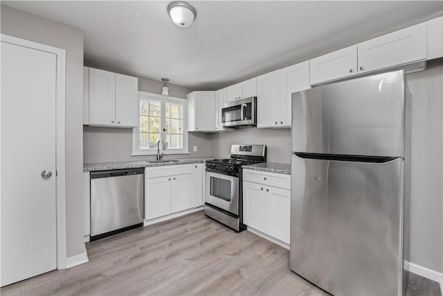 kitchen with stainless steel appliances, white cabinetry, a sink, and light wood-style floors