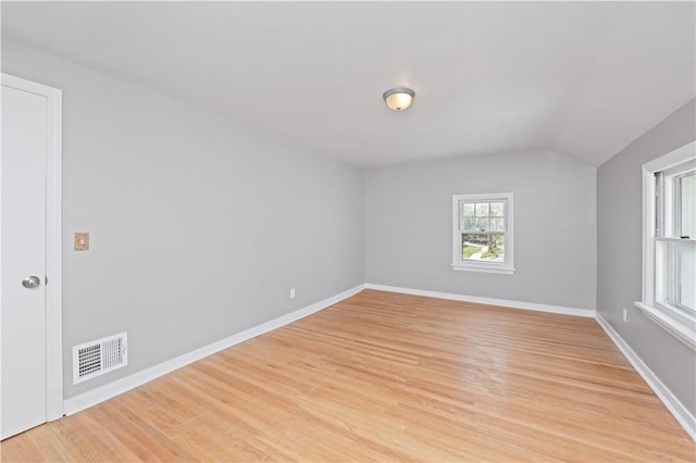 spare room with visible vents, baseboards, light wood finished floors, and lofted ceiling