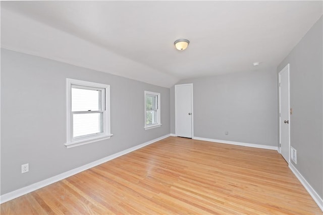 empty room with light wood-type flooring, baseboards, visible vents, and vaulted ceiling
