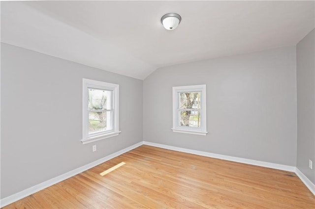 empty room featuring a healthy amount of sunlight, baseboards, vaulted ceiling, and light wood finished floors