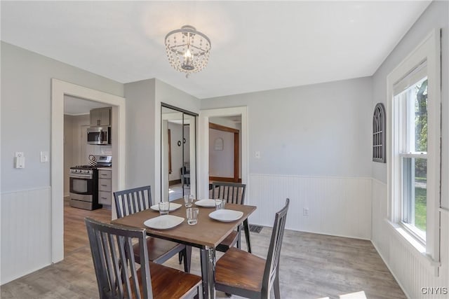 dining area with wainscoting, light wood finished floors, and a notable chandelier