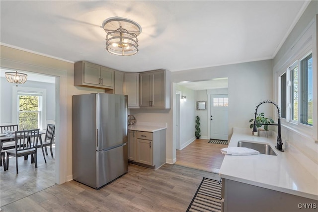 kitchen featuring freestanding refrigerator, a healthy amount of sunlight, a sink, a notable chandelier, and gray cabinetry