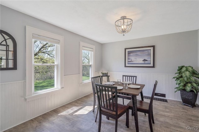 dining area featuring a chandelier, wood finished floors, and a wainscoted wall