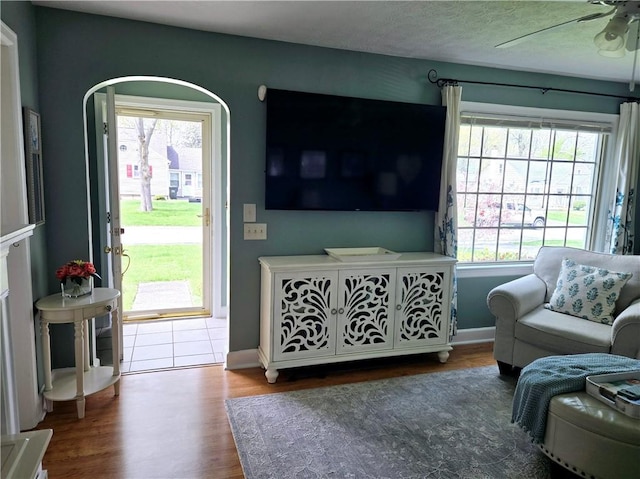 living area with baseboards, a ceiling fan, arched walkways, and wood finished floors