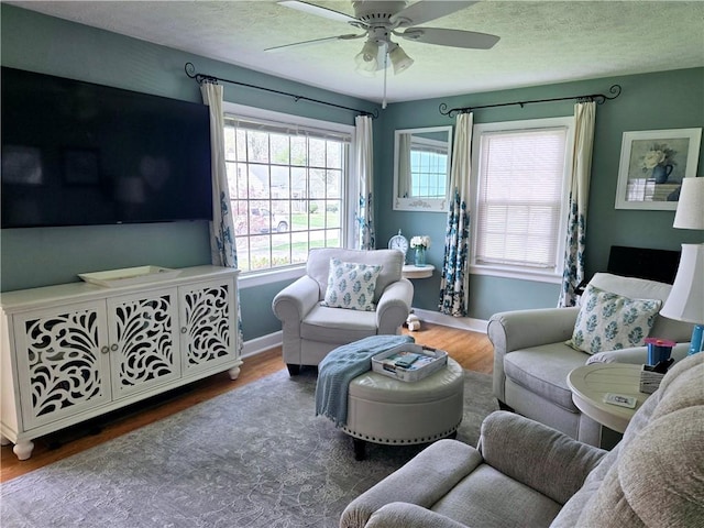 living area with a ceiling fan, baseboards, wood finished floors, and a textured ceiling