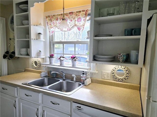 kitchen featuring white dishwasher, open shelves, a sink, light countertops, and white cabinetry
