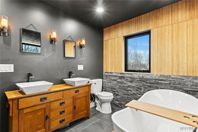 bathroom featuring toilet, double vanity, a freestanding tub, and a sink