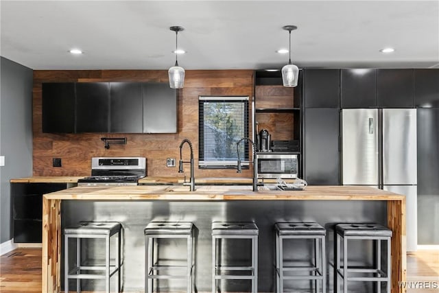 kitchen with baseboards, a kitchen bar, dark cabinets, wood counters, and stainless steel appliances