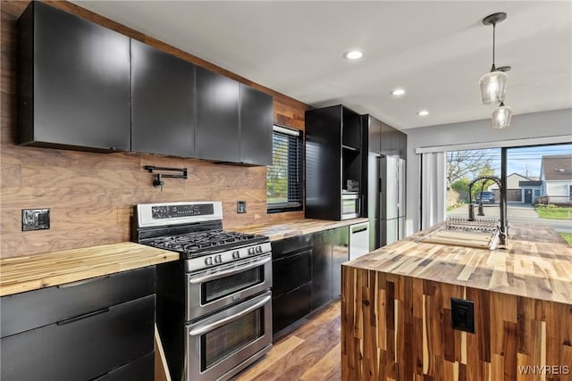 kitchen featuring dark cabinets, stainless steel appliances, butcher block counters, and a sink