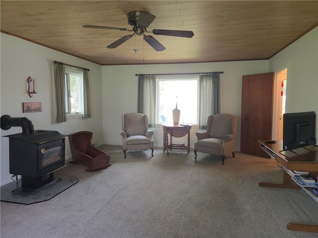 sitting room with wood ceiling, a ceiling fan, a wood stove, and carpet flooring