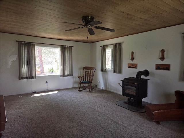 living area featuring carpet flooring, a ceiling fan, a wood stove, and wooden ceiling