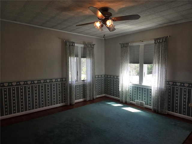 empty room with crown molding, ceiling fan, visible vents, and wood finished floors