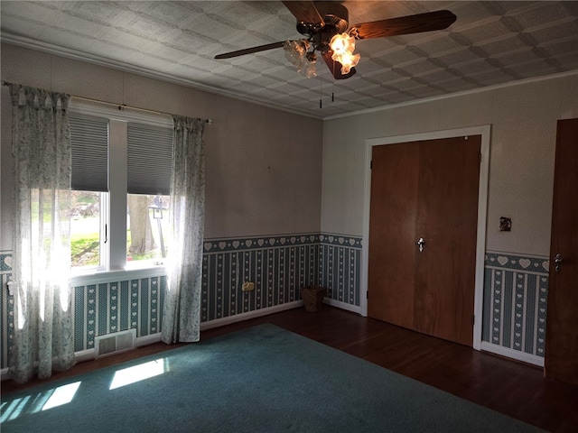 unfurnished room with visible vents, ornamental molding, wood finished floors, ceiling fan, and carpet flooring