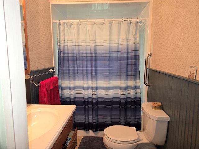 full bath with wainscoting, a shower with shower curtain, toilet, and wallpapered walls