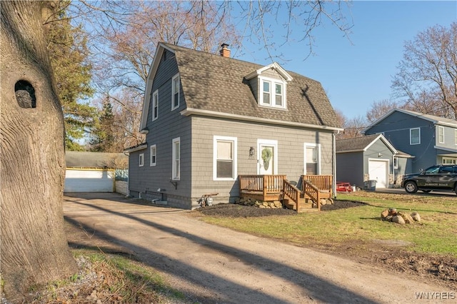 view of front of house with a shingled roof, an outbuilding, a chimney, and a detached garage