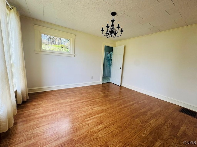 unfurnished room featuring baseboards, visible vents, wood finished floors, and a notable chandelier
