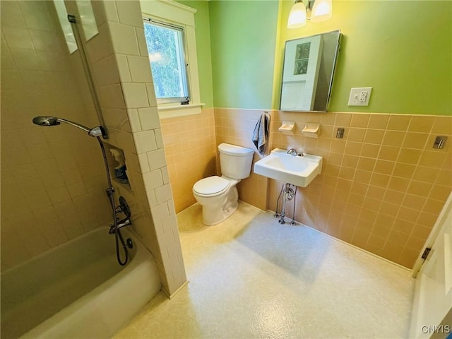 full bath with tile walls, wainscoting, a sink, toilet, and  shower combination