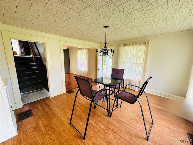 dining area featuring an inviting chandelier, visible vents, baseboards, stairway, and light wood finished floors